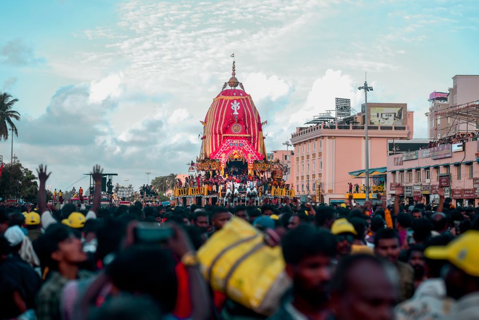 A colorful and lively street festival featuring a decorated chariot surrounded by a large 