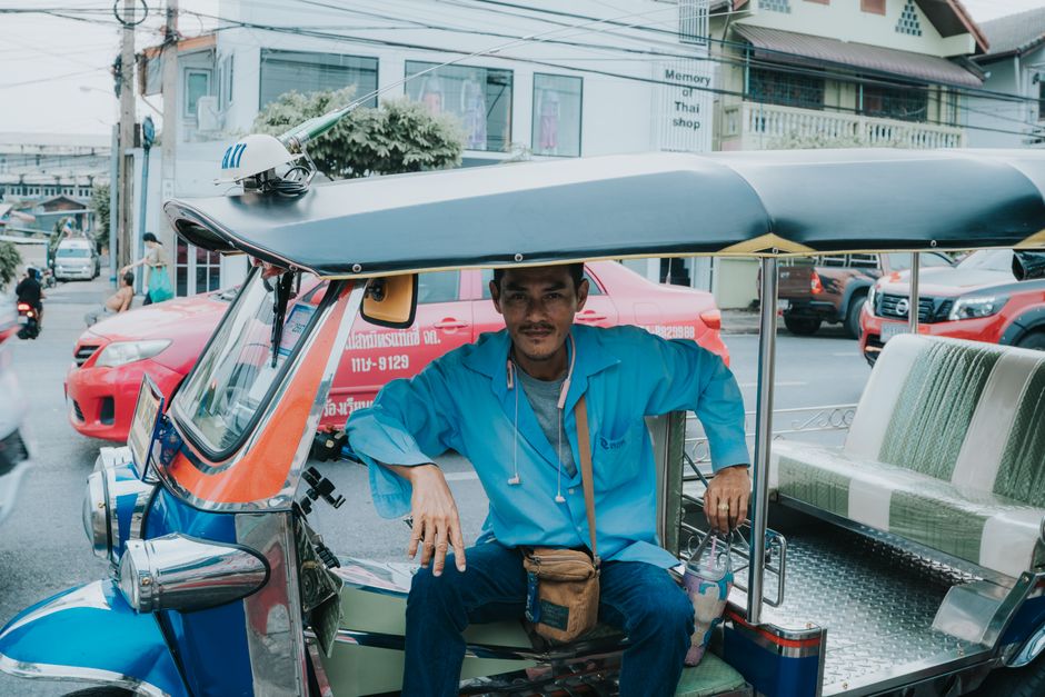Tuk-tuk driver in blue shirt waits on busy Bangkok street, Thailand.