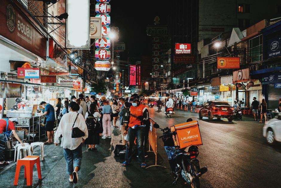 Crowds explore street food and shops in a bustling Chinatown market at night.