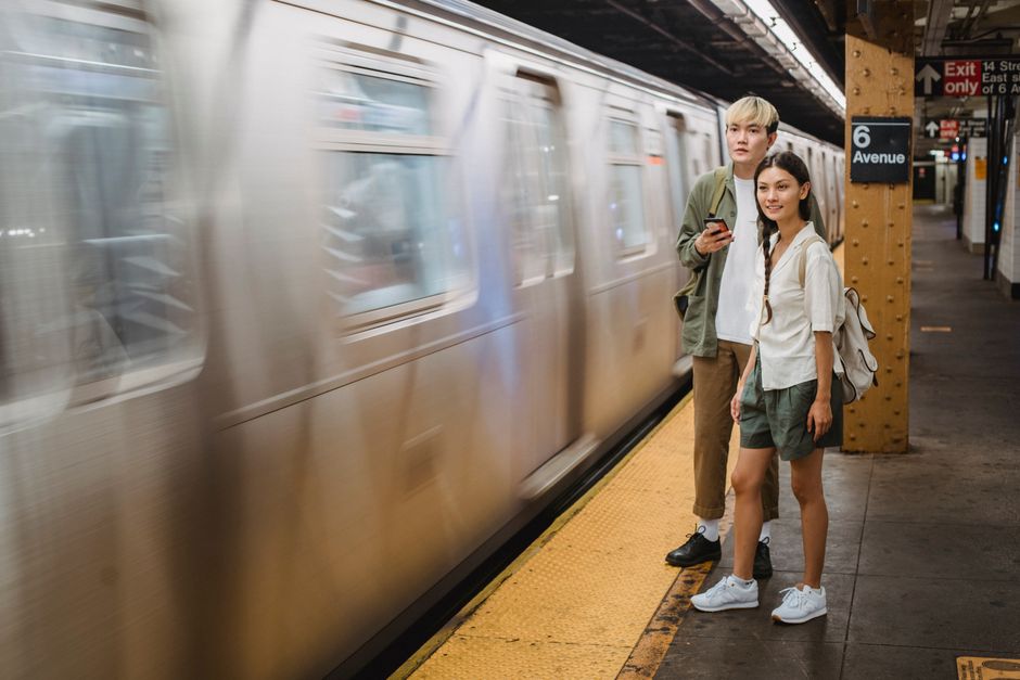 Full length of young stylish Asian couple standing metro station platform and looking at riding train