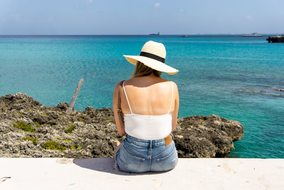 Woman with sun hat sitting by the ocean in George Town, Cayman Islands, enjoying the tropical scenery.