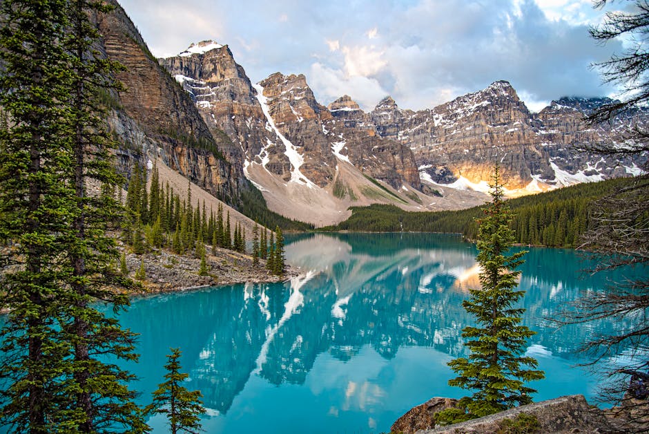 Breathtaking view of Moraine Lake with reflection of snow-covered mountains, pine trees, and vibrant blue water.