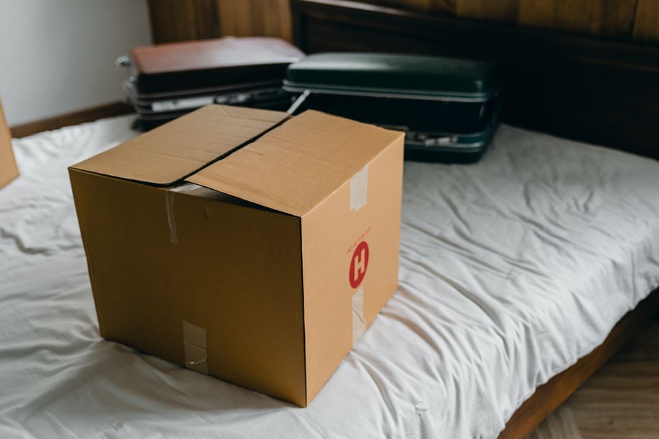 From above of cardboard package placed on bed near suitcases before unpacking belongings after moving in new home
