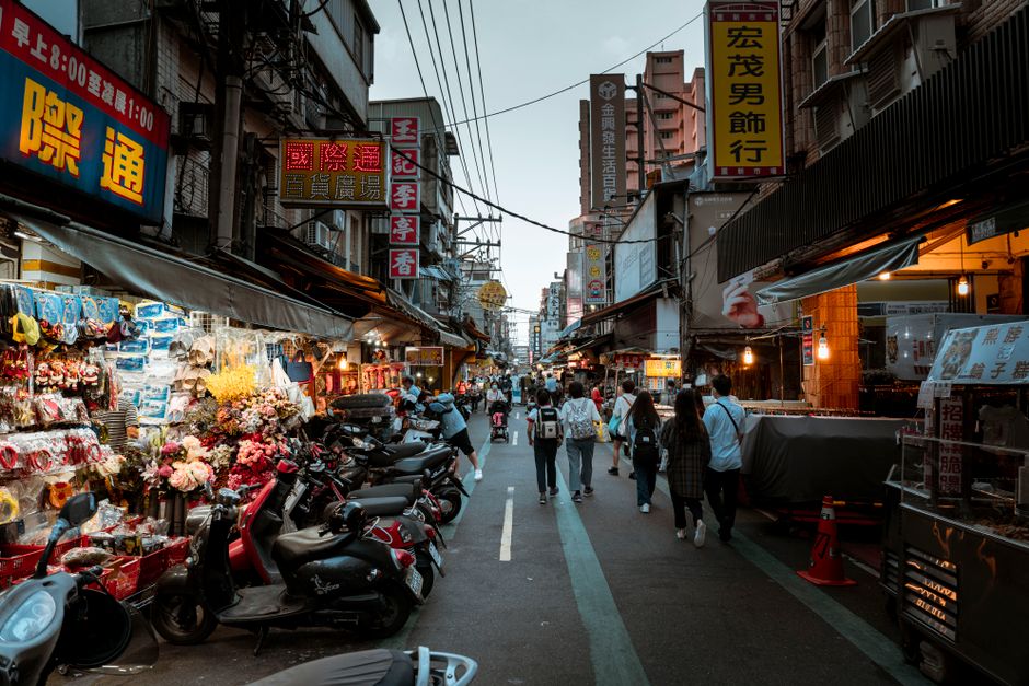 Bustling Asian city street scene with shops, pedestrians, and scooters in a lively urban s
