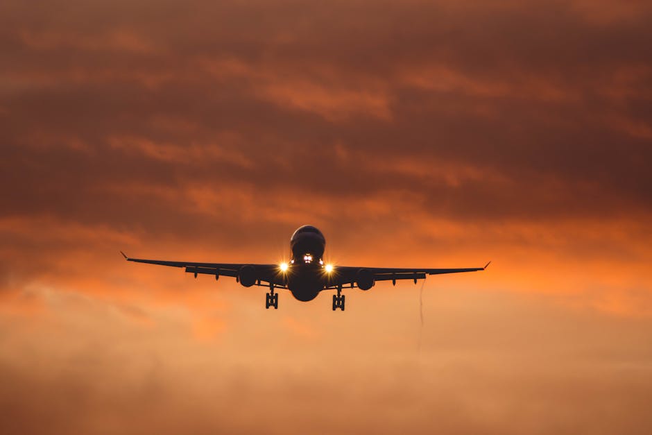 Airliner flying through an orange sky at sunset, creating a dramatic silhouette.