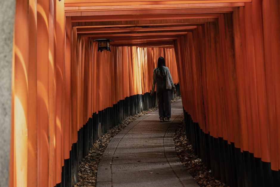 A woman walks through the iconic orange torii gates at Fushimi Inari Taisha in Kyoto, Japan, highlighting its cultural beauty.