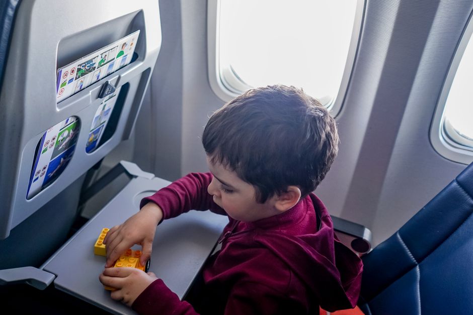 From above side view of boy playing with constructor and sitting on passenger seat while flying on plane during trip