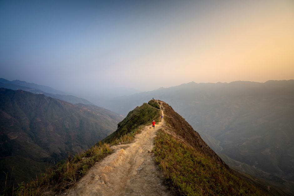 Distant person standing on narrow pathway on hilltop located in spacious breathtaking moun