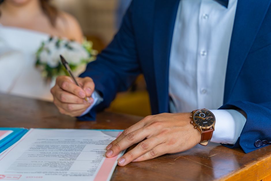 Close-up of groom signing wedding documents with bride nearby.
