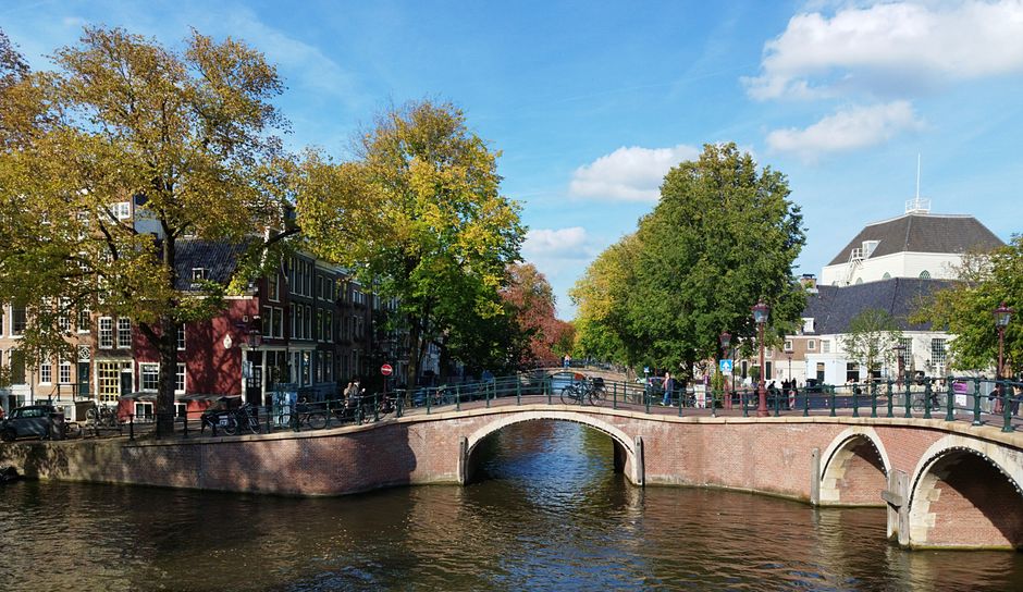 Picturesque view of an Amsterdam canal bridge surrounded by autumn trees and historic buildings.