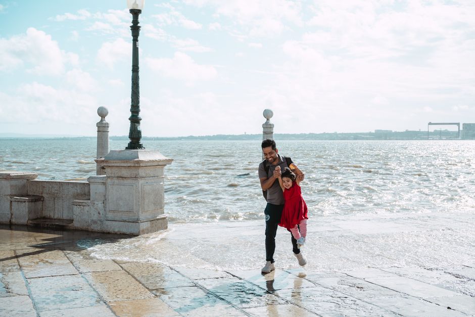 A father playfully lifts his daughter as they enjoy a sunny day by the ocean.