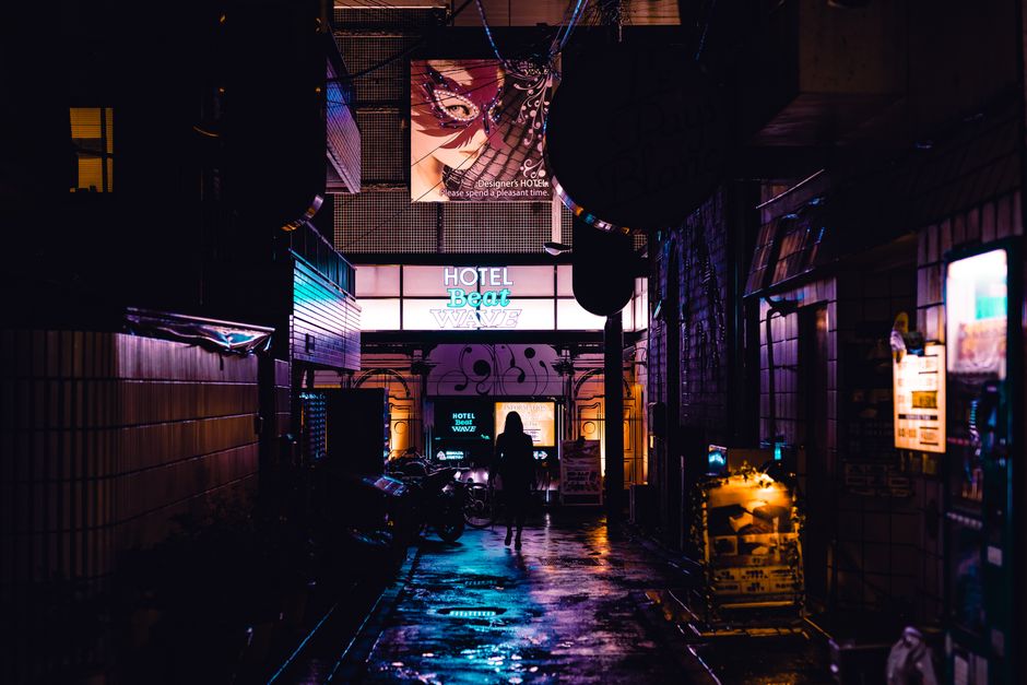 Silhouette of a person walking in a vibrant, neon-lit alleyway in Shinjuku, Tokyo at night.