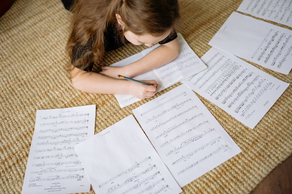 A young girl lying on a carpet writing music notes surrounded by sheets, enjoying a creative moment at home.