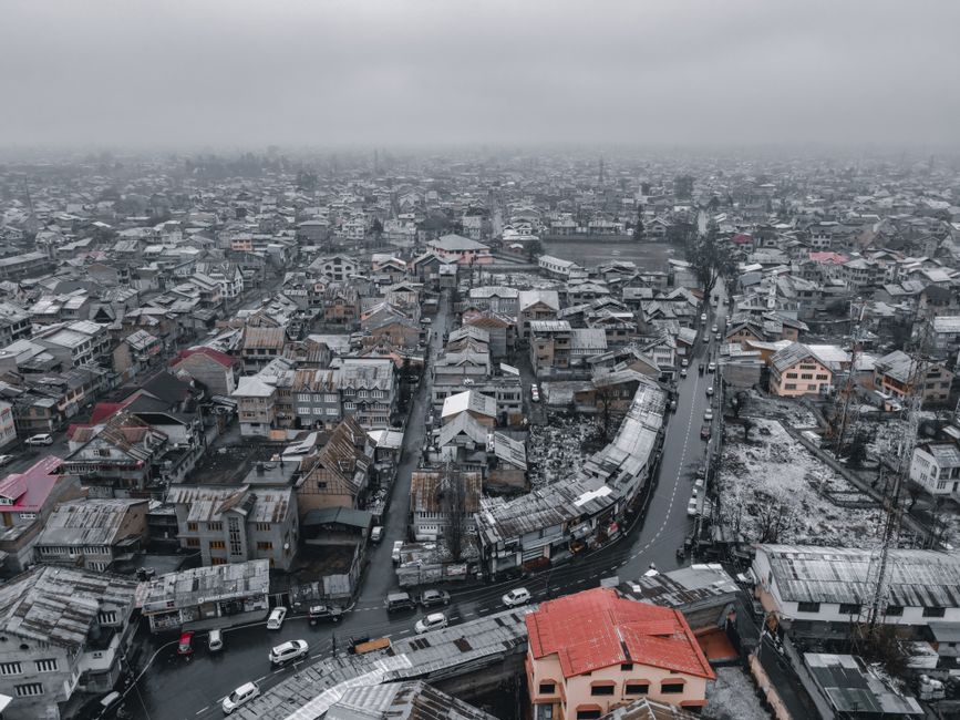 Aerial view of snowy Srinagar cityscape, showcasing rooftops and winding roads in winter.