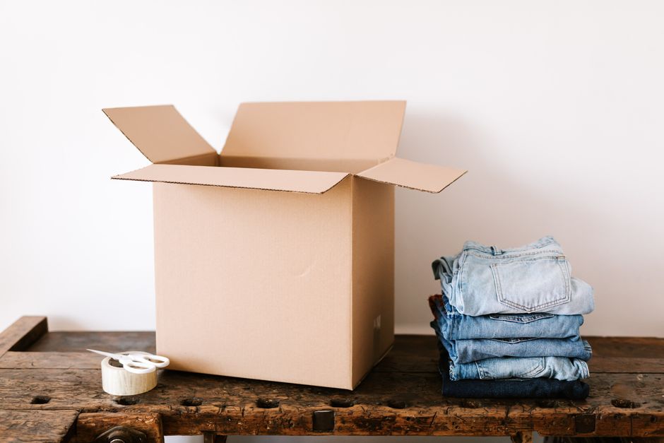 Stacked modern jeans placed near opened cardboard box and tap with scissors before packing for moving out in daylight