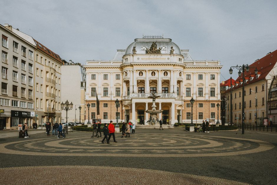 View of the historic National Theatre in Bratislava with pedestrians in the city square.