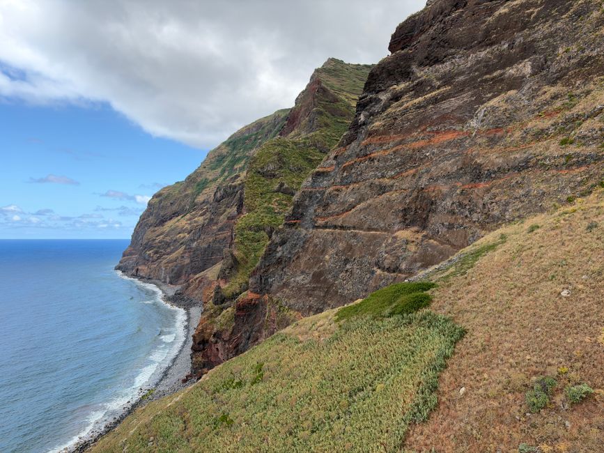 Stunning aerial view of rugged coastal cliffs against the blue ocean and cloudy sky.