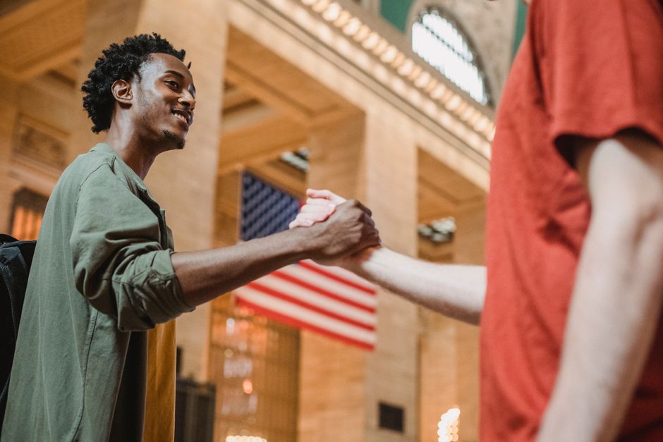 Side view of happy young multiethnic men in casual clothes standing in historic building while shaking hands