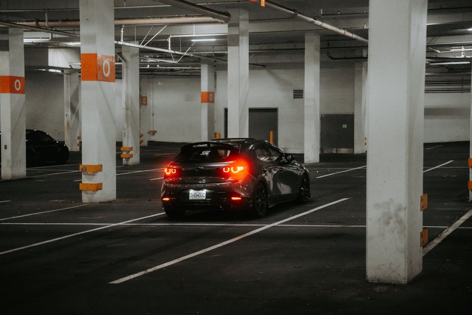 A black car with bright taillights parked in a dimly lit underground garage.