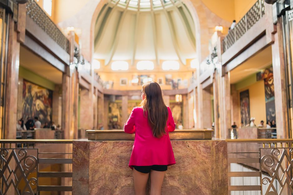A woman in a pink jacket explores an Art Deco interior in Mexico City.