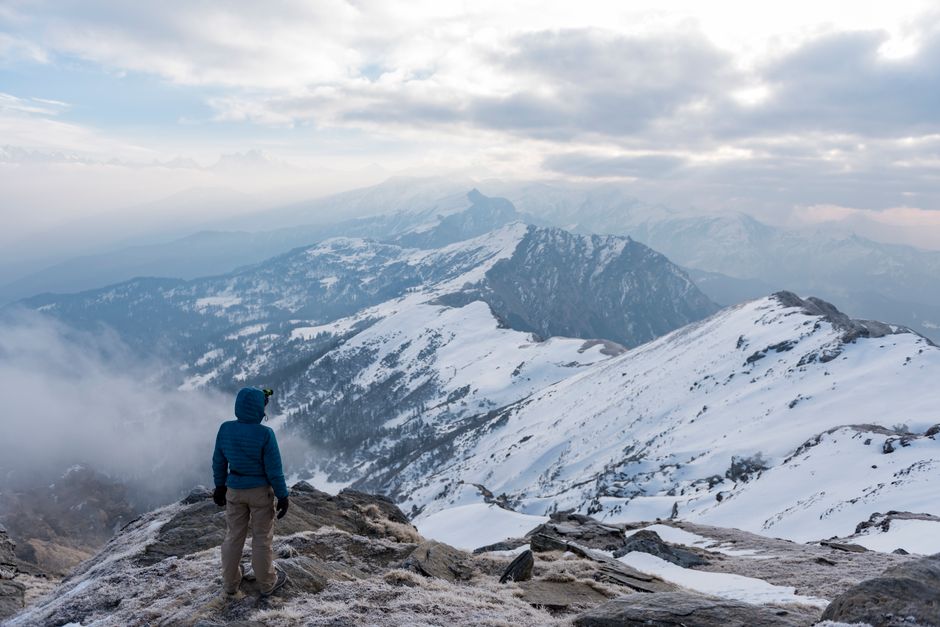 A lone traveler at a snowy mountain peak, embracing a breathtaking winter landscape.