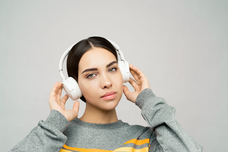 Portrait of a woman in a gray sweater, listening to music with white wireless headphones.