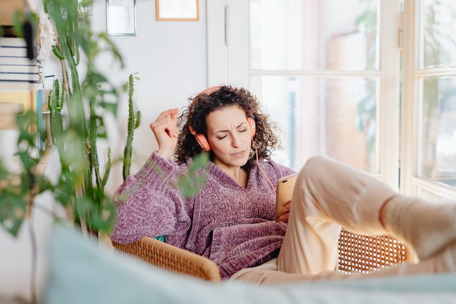 A woman relaxes indoors, listening to music with headphones, enjoying leisure time.