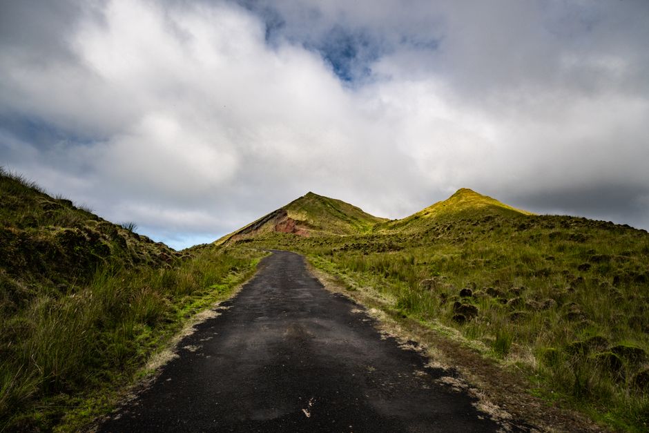 A picturesque road leads to grassy hills under a cloudy sky, capturing the tranquility of nature.