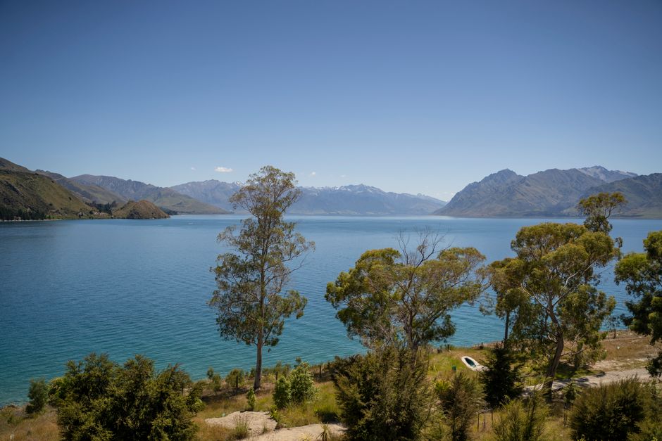 Scenic landscape of Lake Wānaka with clear blue sky and majestic mountains in Otago, New Zealand.