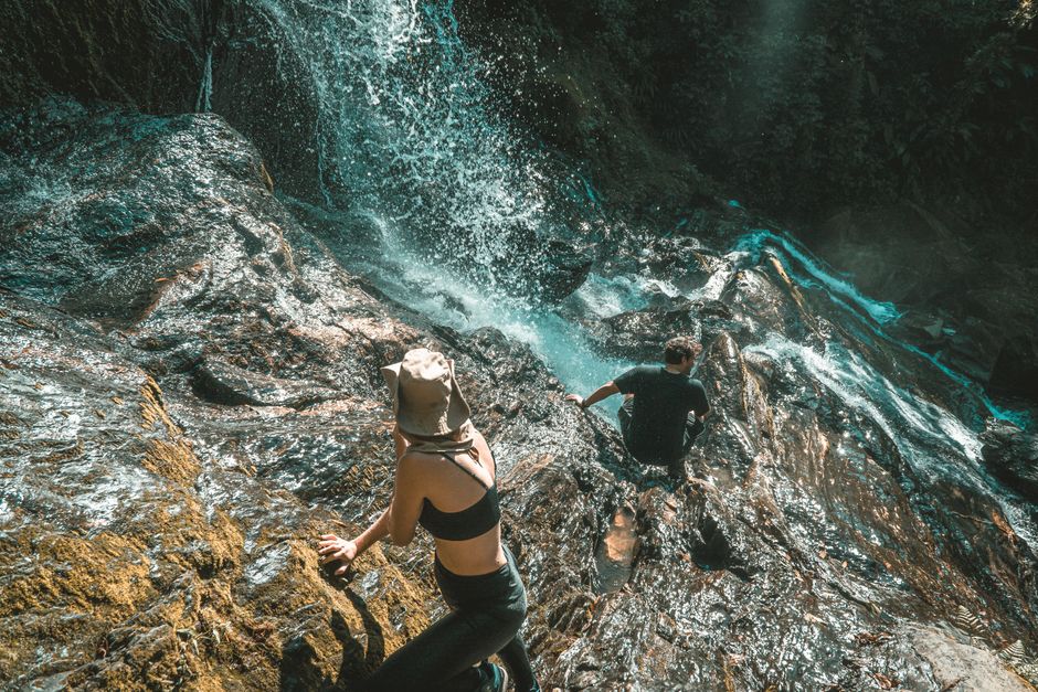 Two adventurers scaling a rocky waterfall, experiencing nature's thrill.