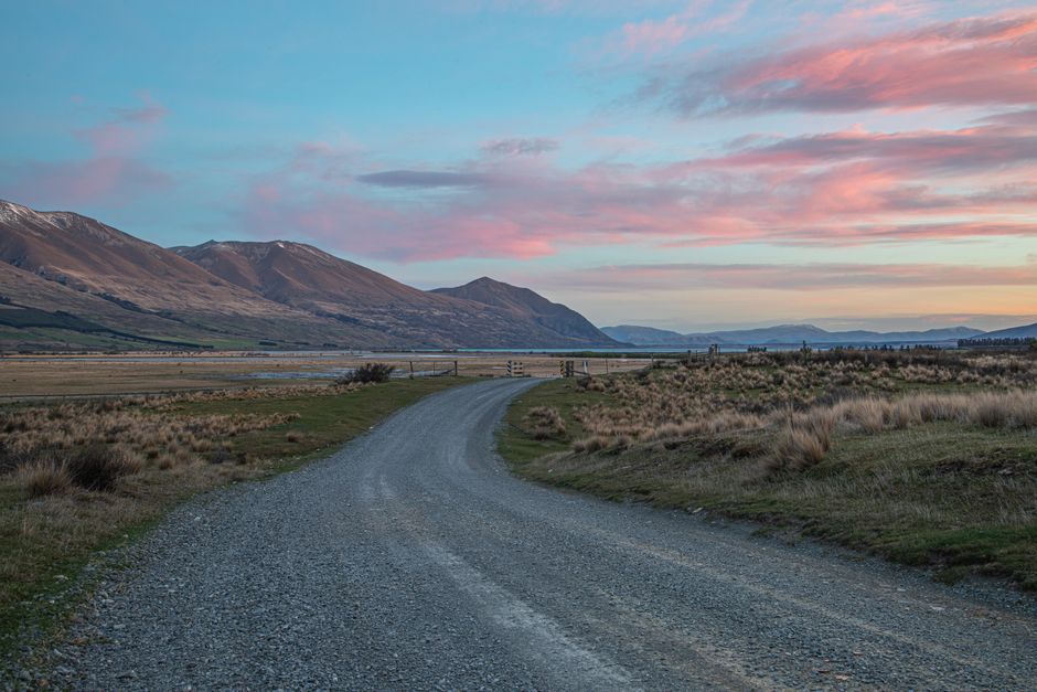 Dirt road winding through serene rural countryside at dusk with colorful sky.