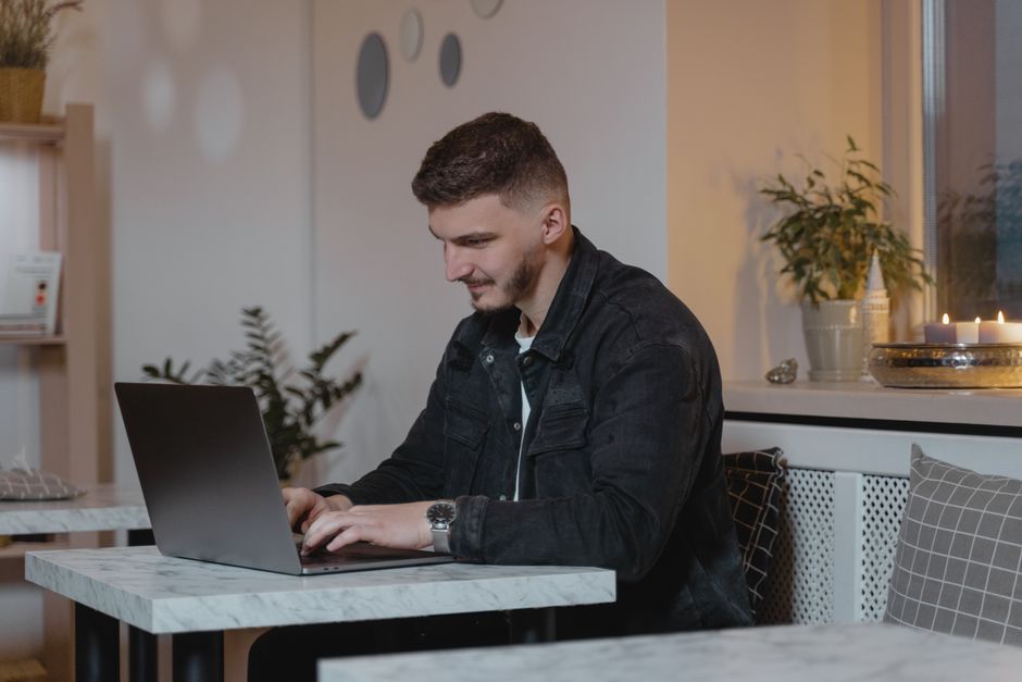 Caucasian man working on a laptop at a cozy indoor setting, surrounded by plants and candles.