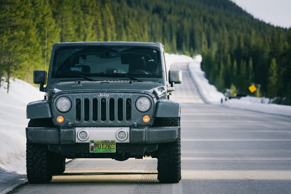 A rugged Jeep parked on a snowy road through dense forest, capturing a sense of adventure.