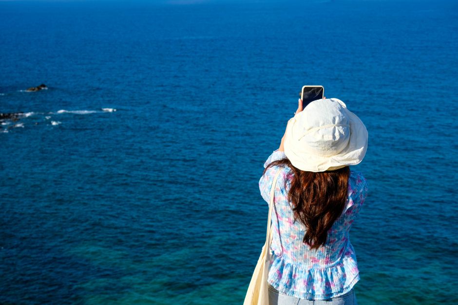 Woman in summer hat capturing the ocean view with a smartphone.