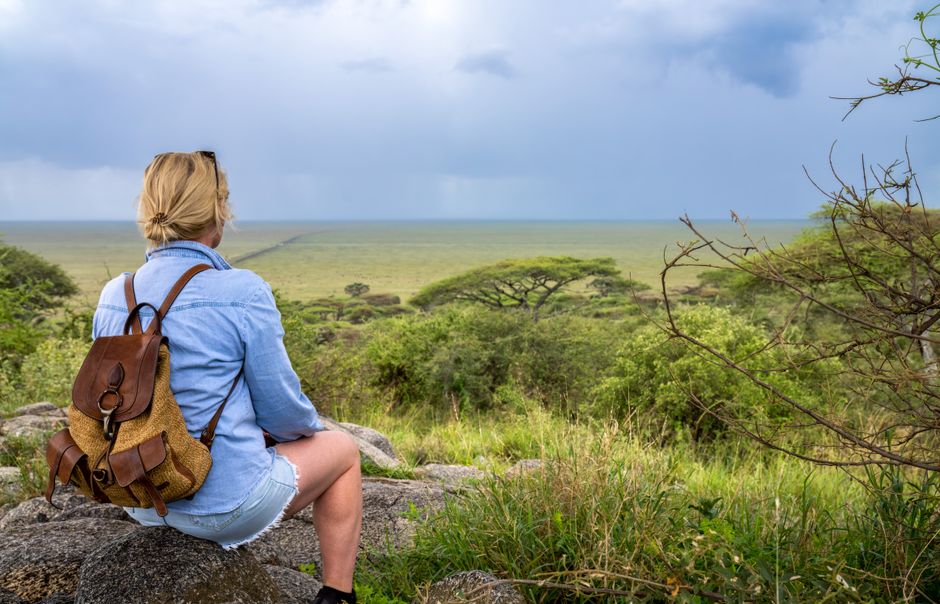 Blonde woman with backpack enjoying view of expansive African landscape under overcast skies.