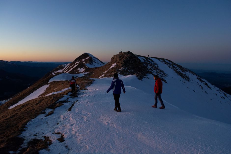 Three people hiking on a snow-covered mountain peak at twilight, capturing a breathtaking 