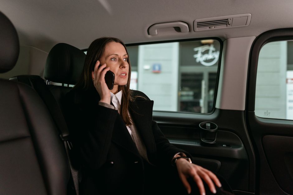 Confident businesswoman talking on phone inside a car. Professional attire, focused expression.