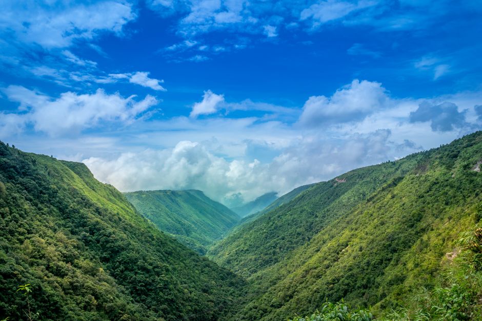 Stunning landscape of a lush green valley under a vibrant blue sky with fluffy clouds.