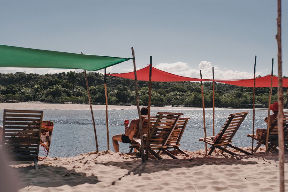 A tranquil scene of people relaxing under colorful sunshades on a sandy beach by the water.