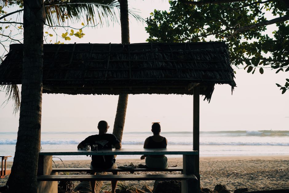 A man and woman enjoying a peaceful moment under a beach hut by the sea.