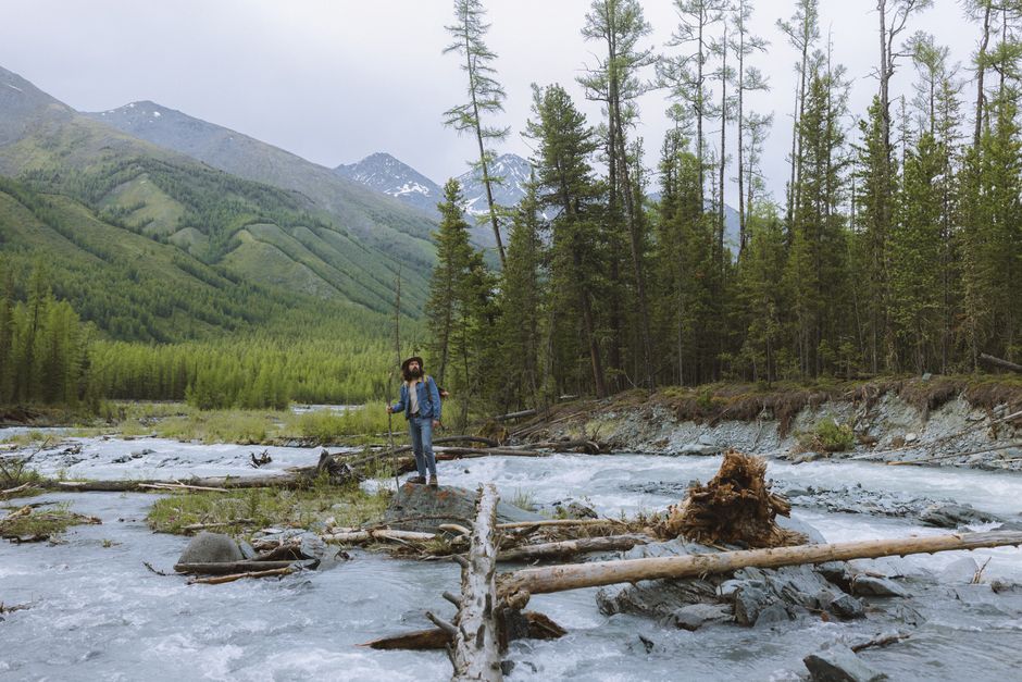 Man in denim explores a scenic mountain river in a lush green forest.