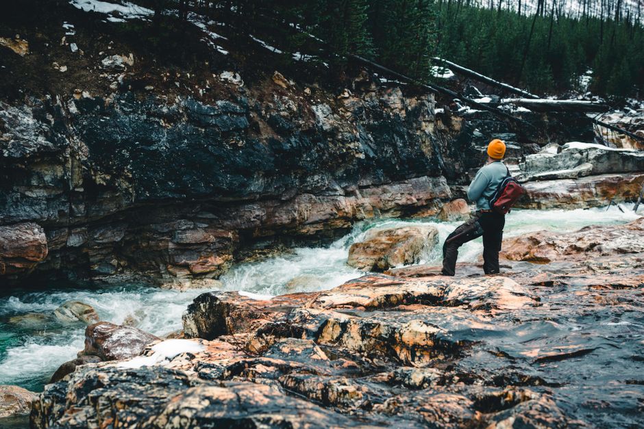 A lone hiker stands by a rushing river in Kootenay Crossing, embracing the wilderness.
